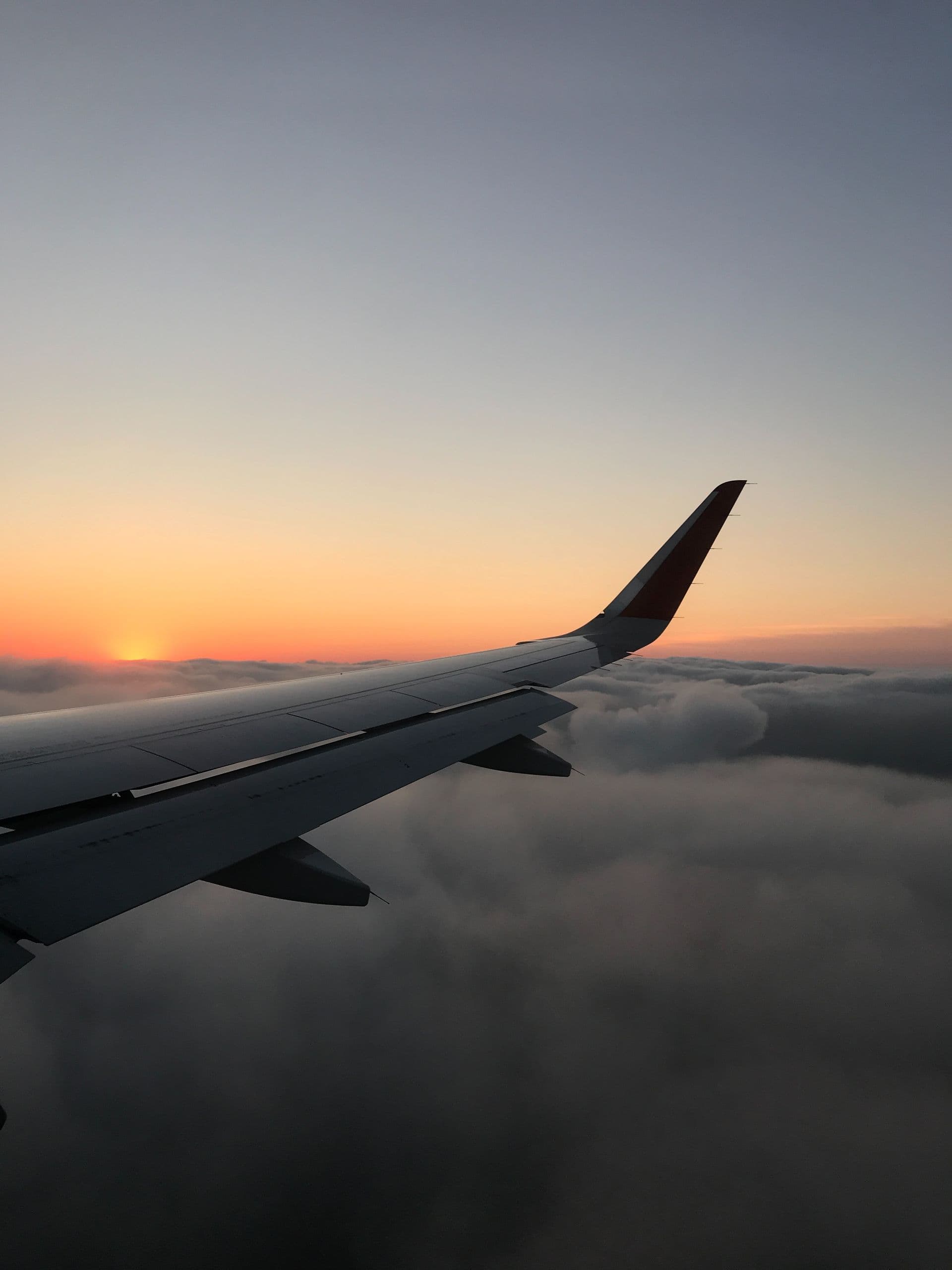 Scenic view from airplane wing at sunset, flying over clouds